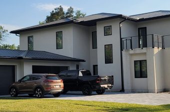 Modern white house with multiple large windows and parked cars.