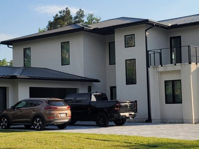 Modern white house with multiple large windows and parked cars.