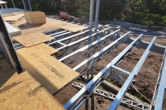 Partially constructed roof with metal trusses and wooden sheathing under clear sky.