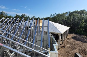 Construction site showing roof framework and steel trusses under clear sky.