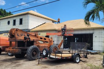 Workers installing a thatched roof using a crane and scaffolding.