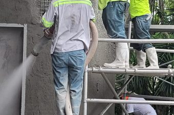 Workers spray-painting a large surface outdoors.