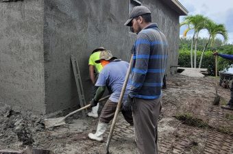 Two construction workers smoothing wet concrete on a floor outdoors.