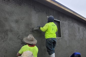 Two workers plastering an exterior wall of a building.