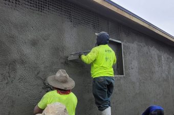Two workers plastering an exterior wall of a building.