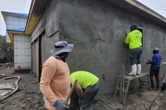 Workers plastering a building's exterior wall.