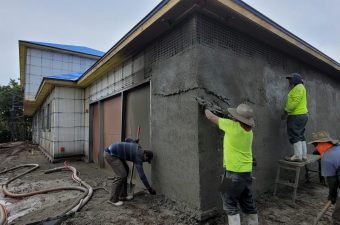 Two workers plastering the exterior wall of a building under construction.