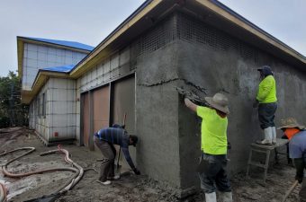 Two workers plastering the exterior wall of a building under construction.