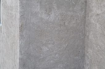 Empty gray concrete wall corner with a small electrical outlet.