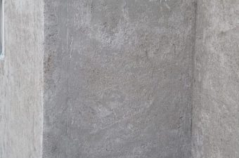 Empty gray concrete wall corner with a small electrical outlet.