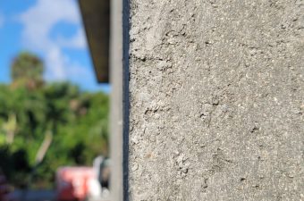 Close-up of a textured concrete wall edge with blurred outdoor background.