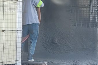 Worker spraying concrete onto a wall for construction.