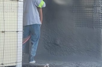 Worker spraying concrete onto a wall for construction.