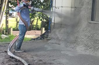 Worker spraying concrete onto a wall using a hose.