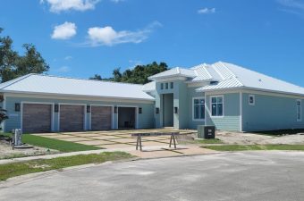 Modern single-story house with light blue exterior and white roof under a clear sky.