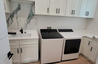 Modern laundry room with washer, dryer, and sink under white cabinets.