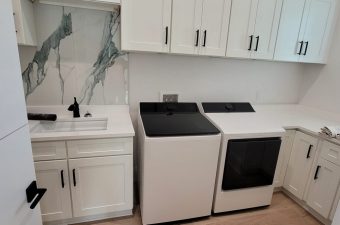 Modern laundry room with washer, dryer, and sink under white cabinets.