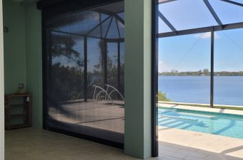 View of a screened patio with a pool and lake beyond on a sunny day.