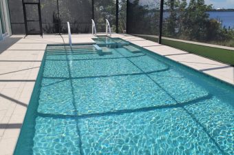 Clear swimming pool with a pool cover partially removed under bright sunlight.