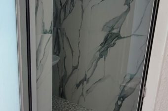 A small shower area with marble-patterned walls and pebble floor.