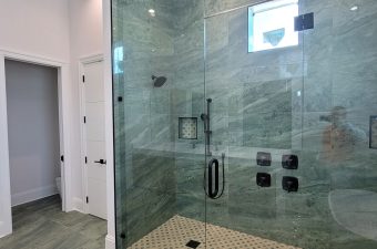 Modern glass walk-in shower with marble walls and black fixtures.