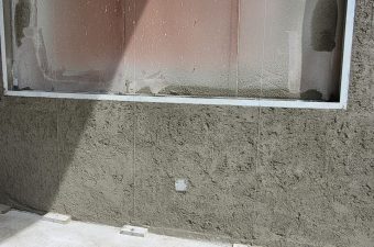 Freshly applied cement plaster on a wall surface near a window.