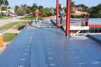 Workers installing metal roofing panels on a building under construction.