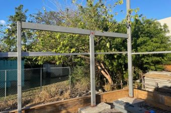 Metal railing structure under construction in a garden area.