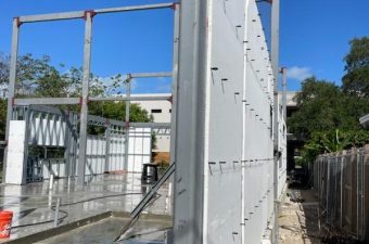 Construction site with metal framing and white panels under clear sky.