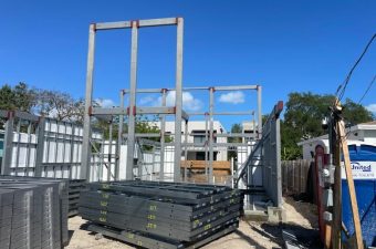 Construction site with steel frames stacked against a structure under a clear blue sky.