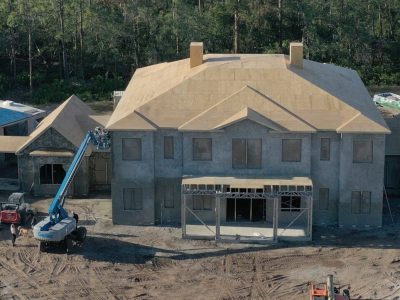 A large unfinished house under construction with scaffolding and a crane.
