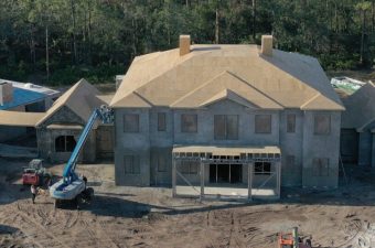 A large unfinished house under construction with scaffolding and a crane.