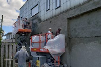 Workers plastering a building wall using a lift platform.