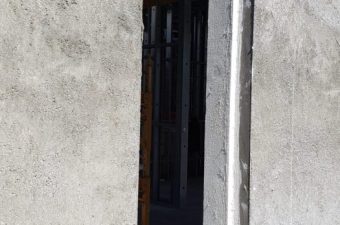 Narrow gap between two concrete walls revealing a dark interior space.