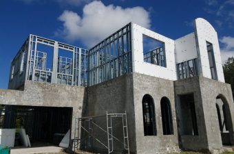 Partially constructed building with concrete walls and steel framing under a blue sky.