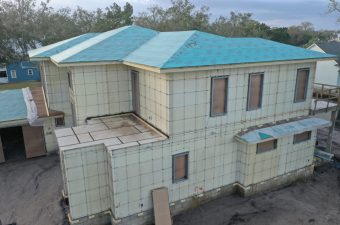 Two-story house under construction with blue roof and tiled walls.