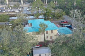 A house with a bright blue roof surrounded by trees and vehicles.