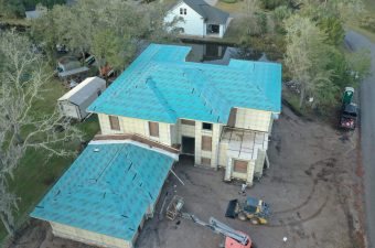 A house with a newly installed blue roof under construction.