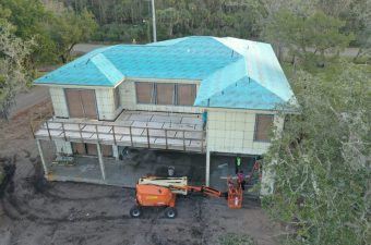 A house elevated on stilts with a blue roof under construction.
