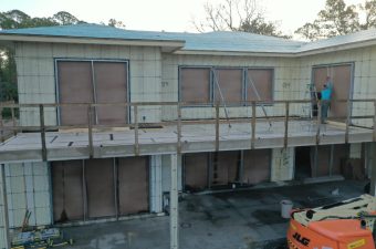 A building under construction with boarded windows and a scaffolding platform.