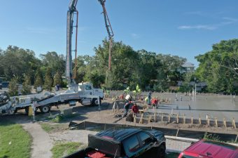 Workers pouring concrete on a sunny construction site with trucks and equipment.