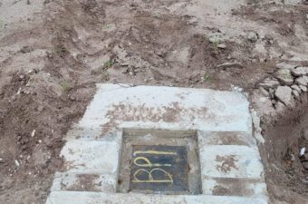 Grave marker with initials on muddy ground.