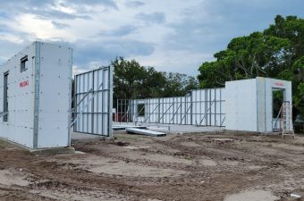 Construction site with partially built white walls and open metal gate.
