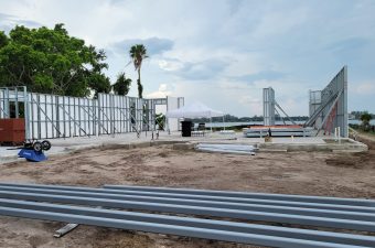 Construction site with metal beams and a waterfront view under a cloudy sky.