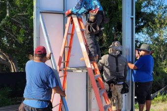 Workers assemble a large structure outdoors on a sunny day.