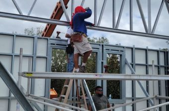 Worker on scaffold guiding steel roof truss