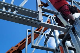 Worker in safety gear assembling metal framework under blue sky.