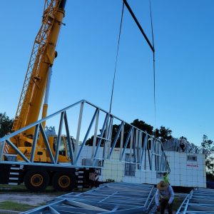 A crane lifts a metal bridge structure at a construction site.