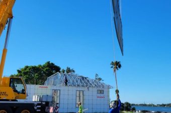 Workers use cranes to lift a metal roof frame onto a house.