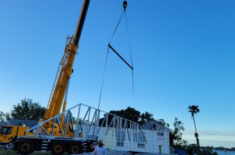 Crane lifting a large white container against a clear blue sky.